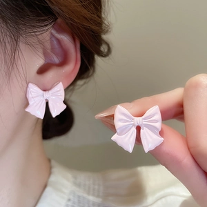 Close-up of pink bow earrings on ear and hand showing glossy finish and size