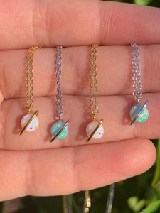 Detailed view of gold and silver opal planet necklaces held in natural sunlight
