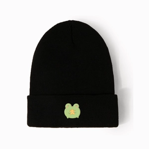 Detail view of a black knitted beanie featuring a cute frog holding a yellow star emblem