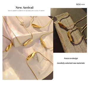 Detailed view of gold twist bar pendant on a sleek snake chain over artistic background