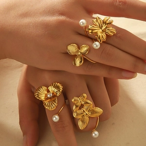 Butterfly and flower 18k gold plated rings with pearls on hand against a sandy background