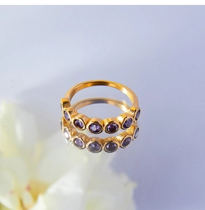 Dettaglio anello in titanio placcato oro 18K con zirconi viola su superficie riflettente