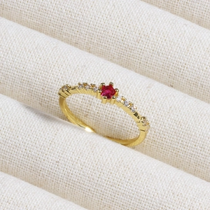 Macro detail of gold ring featuring a red gemstone and clear zircon on textured fabric