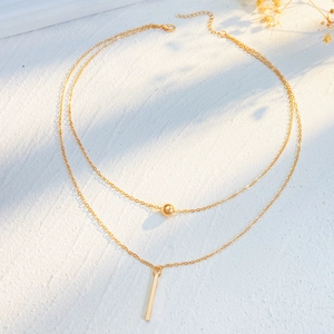 Macro detail of gold layered necklace featuring a vertical bar pendant and bead accent