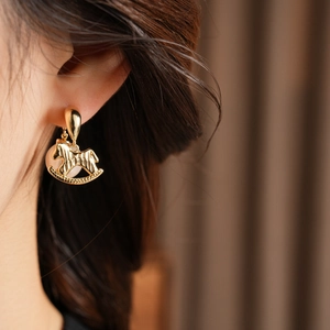 Détail de la boucle d'oreille cheval à bascule doré et perle portée par le mannequin