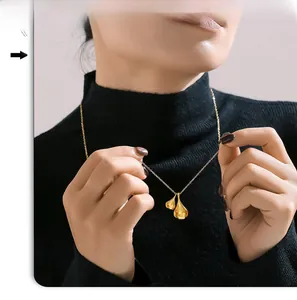 Polished gold double teardrop pendant necklace worn on a black turtleneck sweater