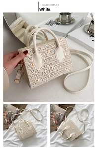 Detail of white straw bag with daisy embroidery, featuring top handles and shoulder strap