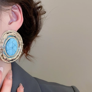 Dettaglio di modella che indossa orecchini ovali blu vintage con montatura dorata