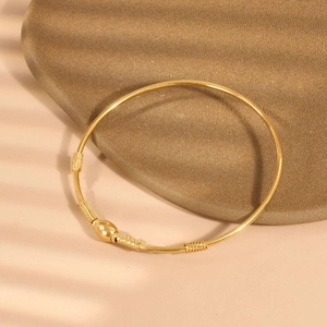Detail eines goldenen Armreifs mit gedrehtem Draht und ovaler Perle auf Stein