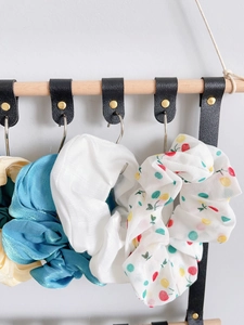 Hanging display of satin scrunchies on a wooden wall organizer with leather straps
