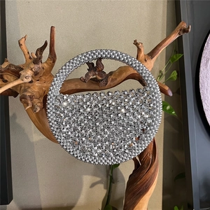 Close-up of a silver beaded crescent bag with round top handle on a rustic wooden stand