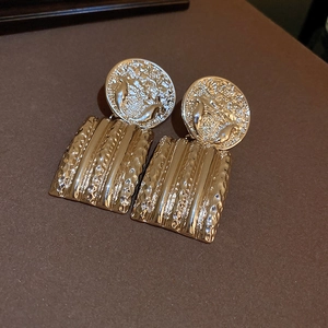 Detailed macro of vintage gold earrings with coin relief and textured rectangle charms