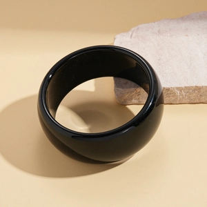Polished wide black resin bangle displayed with natural stone on neutral background