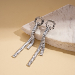 Close-up of silver tassel earrings with zircon stones on a decorative beige stone