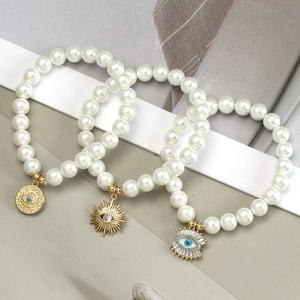 Three white pearl bracelets with golden evil eye pendants decorated with blue crystals
