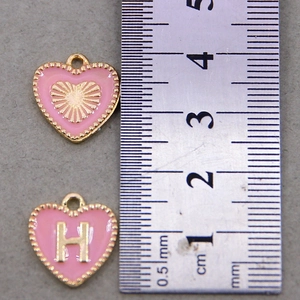 Pink heart pendant with golden letter H shown next to a ruler for size reference