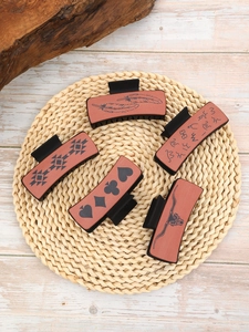 Detail view of five brown leather hair claw clips with various Western cowboy patterns