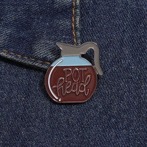 Close-up of red and blue coffee pot enamel pin with 'POT head' text on denim jacket
