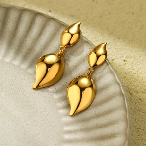 Macro detail of high-polish 18K gold teardrop earrings on a textured ceramic surface