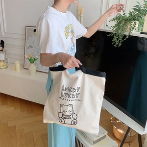Detail of canvas tote bag featuring black embroidered bear and lucky text decoration