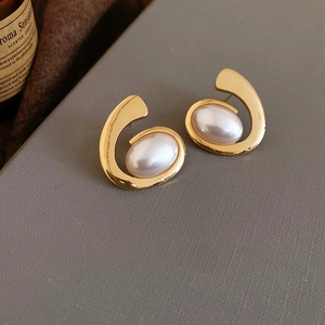 Detail of gold-plated oval stud earrings with wrap-around pearls on a soft leather surface