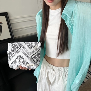 Detail of floral paisley makeup bag being held by a model in a casual indoor setting