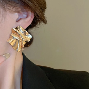 Detail of gold-plated irregular pleated square stud earrings worn by a model