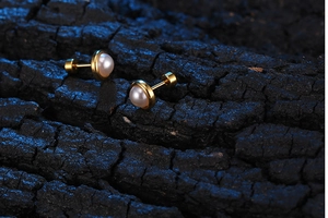 Macro shot of minimalist gold pearl stud earrings on a textured black charcoal background