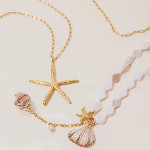 Close-up of shell, conch, and pearl pendant necklaces with golden textures on beige surface