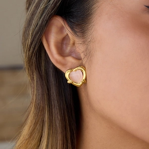 Detail shot of a sweet pink heart earring in a gold frame worn on a model earlobe