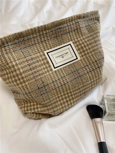 Detail of checkered tweed makeup bag with Pleasant Time label on soft fabric background