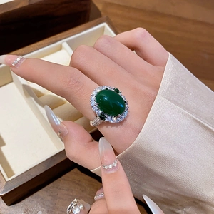 Close-up of a vintage green oval emerald ring with sparkling zircon on a finger