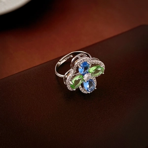 Macro shot of silver flower ring with blue and green gems on dark leather background