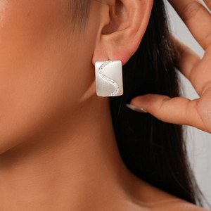 Macro view of a matte silver rectangular stud earring with S-shaped zircon inlay on model