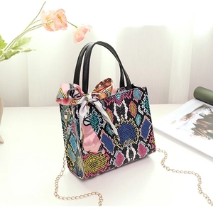 Detail of colorful snakeskin pattern handbag with silk scarf and metal chain strap