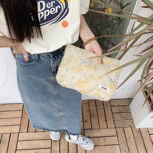 Detail of floral embroidery on a beige cotton pouch held by a model in casual outfit