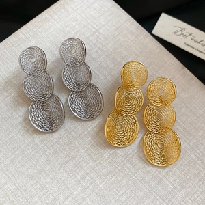 Modern geometric hollow-out round earrings in gold and silver finish on textured fabric