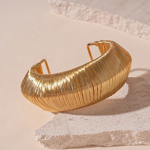 Detail of a wide gold metal cuff bracelet with delicate parallel wire weaving texture