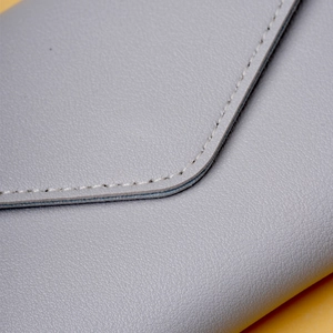 Close-up of light gray pebbled leather texture and neat stitching on a compact wallet