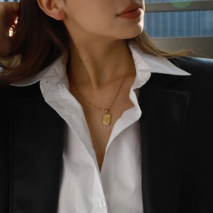 Close-up of a gold angel pendant necklace with crystals on a woman in a leather jacket