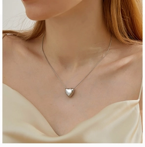 Polished silver heart pendant on a delicate chain worn over champagne silk fabric