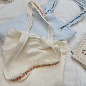 Detail of canvas tote bags with floral embroidered straps in beige and light blue