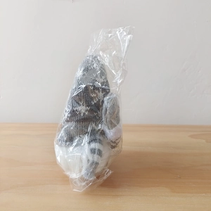Close-up of a grey knitted Christmas gnome with a long beard in protective polybag