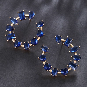Macro detail of gold hoop earrings set with blue heart and drop shaped gemstones