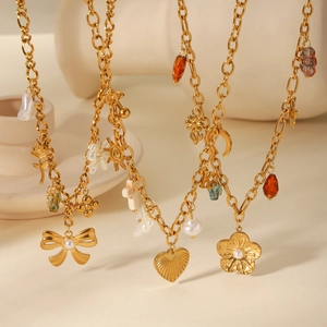 Détail de colliers dorés avec pendentifs nœud, perle, cœur et soleil sur fond beige