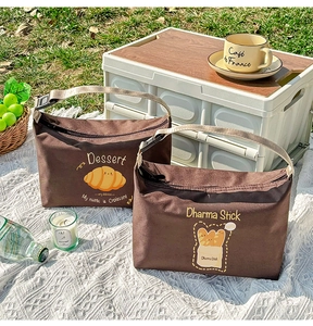 Insulated lunch bags with bread illustrations on grass during an outdoor picnic setup