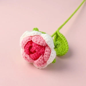 Close-up of handmade crochet rose with pink and white petals and green leaves