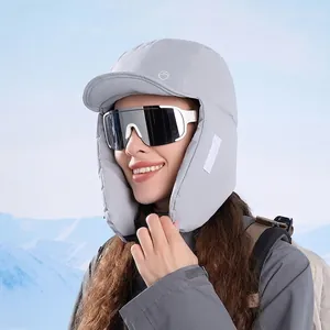 Grey windproof winter trapper hat with ear flaps shown against a snowy mountain backdrop