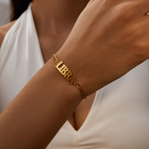 Gold stainless steel Libra zodiac bracelet for women on a model's wrist with white outfit