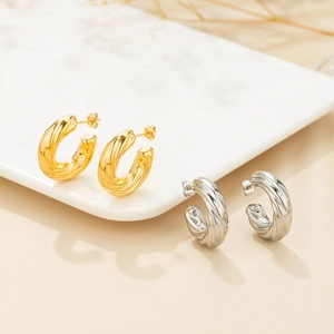 Detail of twisted hoop earrings in gold and silver finish on marble display stand